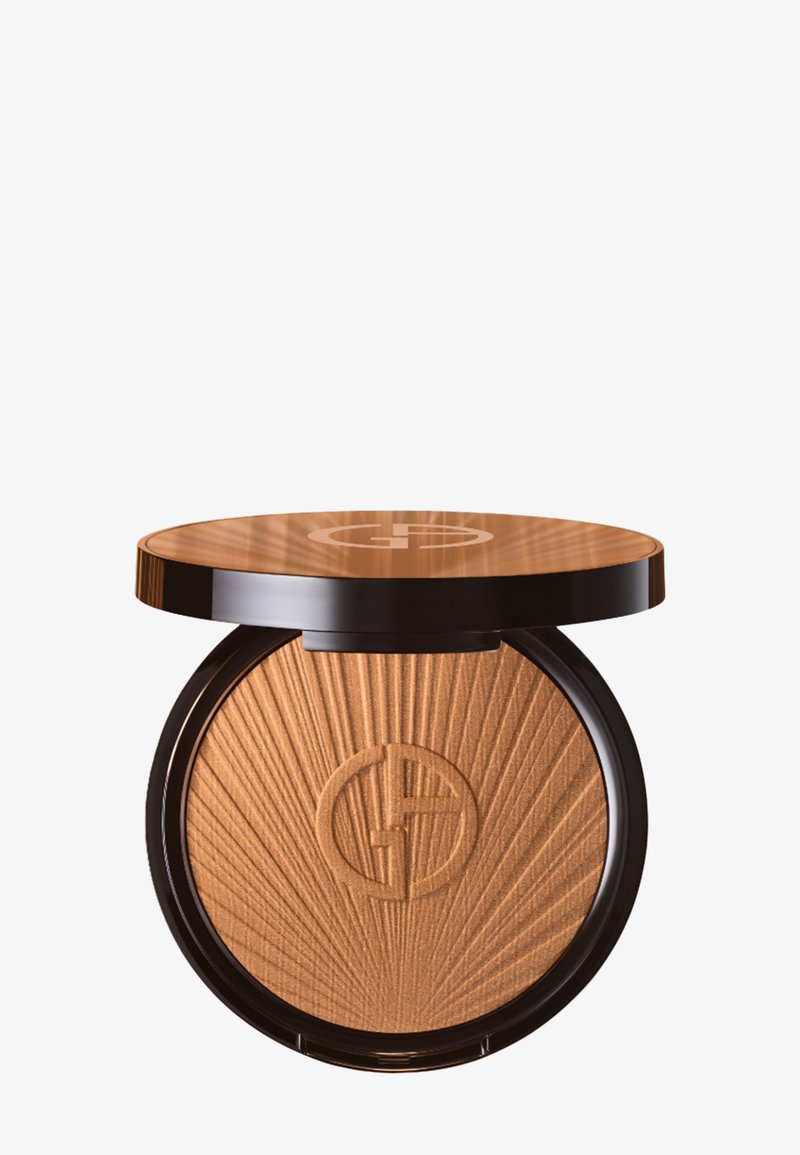 Bronzer-pulver i en rund kompakt. Lysebrun nyanse med solstråle tekstur og gravert logo. Jevn overflate og glansfull brun lokk.