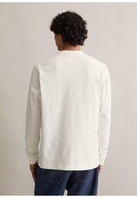 Weißes Langarmhemd aus Baumwolle mit Rundhalsausschnitt und geradem Schnitt. Getragen mit Jeanshosen, zeigt die Rückansicht.