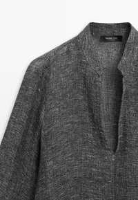 Pull en maille texturée gris foncé avec un col en V profond et des manches longues, étiquette indiquant Massimo Dutti fabriqué au Maroc.