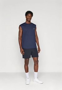 Camiseta desportiva azul-marinho sem mangas combinada com calções escuros. Tecido macio, ajuste descontraído e design minimalista. Ténis brancos e meias até ao meio da canela.