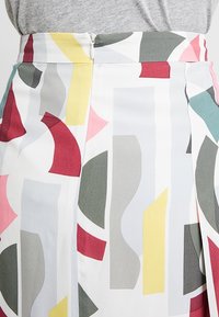 Falda multicolor con patrones geométricos abstractos en rojo, amarillo, gris y verde azulado. Fabricada en una tela suave con cierre de cremallera en la parte trasera.