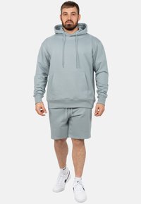 Lichtblauwe hoodie met een buidelzak aan de voorkant, gecombineerd met bijpassende shorts. Witte sneakers met zwarte accenten maken de look af.