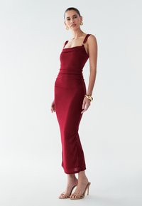 Červené priliehavé midi šaty so štvorcovým výstrihom a nastaviteľnými ramienkami. Hladká látka s nariasenými detailmi, kombinované s telovými sandálmi na opätku so zapínaním okolo päty.