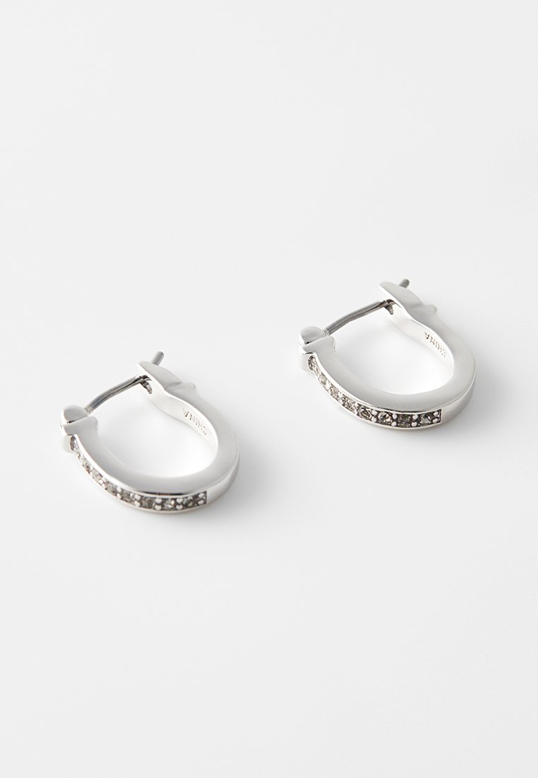 Ein Paar kleine silberne Creolen mit einer Reihe eingearbeiteter, klarer Edelsteine an der äußeren Kurve, vor einem weißen Hintergrund.