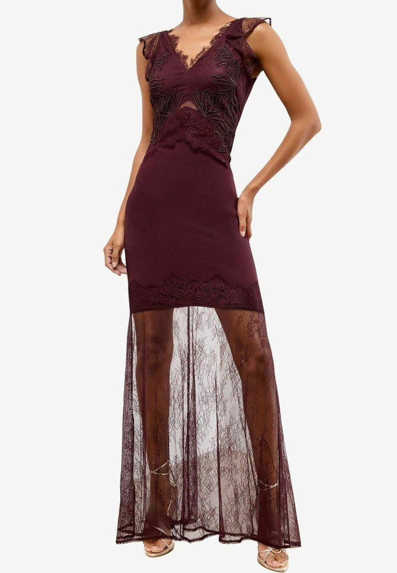 Robe sans manches violet foncé avec corsage en dentelle, découpe au niveau du ventre et superposition de jupe en dentelle transparente s'étendant jusqu'au sol sur une mini-jupe unie.
