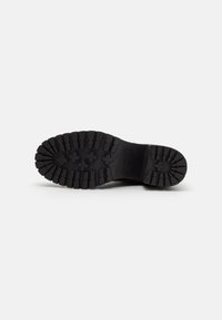 Black rubber shoe sole with deep treads, hexagonal patterns, and a smooth section near the heel; durable and designed for traction.