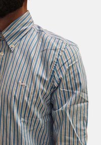 Camicia a righe blu e bianche con colletto a punta e piccolo logo ricamato sul petto, realizzata in tessuto leggero.