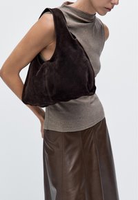 Brown suede handbag with a curved shape and large opening, worn over the shoulder. Accompanied by a fitted brown top and leather skirt.