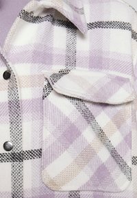 Flanellen shirt in wit met paars en grijs ruitpatroon, voorzien van een borstzak en drukknopen, gemaakt van zachte, gestructureerde stof.