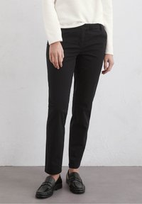 Black tailored pants with a slim fit, smooth texture, and front pockets, paired with black loafers, against a neutral background.
