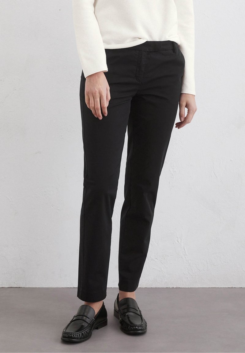 Black tailored pants with a slim fit, smooth texture, and front pockets, paired with black loafers, against a neutral background.