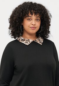 Černý top s dlouhým rukávem a límcem s leopardím vzorem. Měkká textura, volný střih a viditelné kruhové náušnice.
