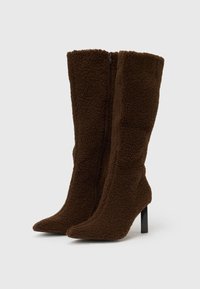 Cizme maro cu toc înalt, realizate din material texturat, cu fermoar frontal și design cu vârf ascuțit.