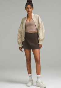 Chaqueta bomber ligera beige, sujetador deportivo marrón, falda ajustada marrón, zapatillas blancas con detalles grises y calcetines a rayas en gris y blanco.