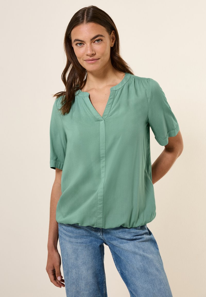 Blusa verde a maniche corte realizzata in tessuto liscio, con scollo a V e vita leggermente arricciata per un fit rilassato.
