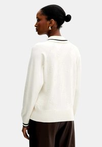 Maglione bianco con un motivo testurizzato, orlo a coste e striscia nera sul colletto. Maniche lunghe, vestibilità comoda e design semplice.