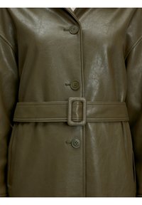 Olijfgroene leren jas met een soepele textuur, voorzien van een ceintuur in de taille, grote knopen en een kraag met punten.