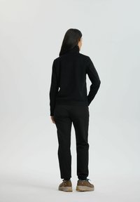 Sort højhalset sweater med lange ærmer; struktureret stof. Kombineret med sorte bukser og lysebrune vandresko. Minimalistisk design.