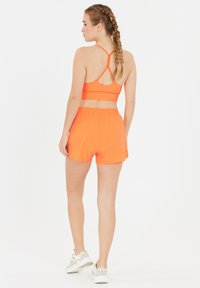 Ljusorange sportbh med racerback-design, kombinerad med matchande orange shorts som har resårmidja och en avslappnad passform.