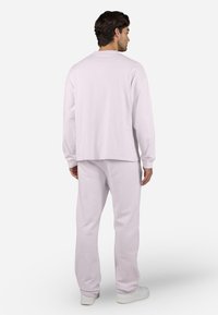 Camisa de manga larga de color rosa claro y pantalones de chándal a juego, fabricados en un tejido suave. El conjunto tiene un corte relajado con puños acanalados y cuello redondo.