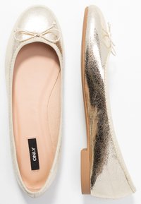 Guldmetalliska balettlägenheter med en texturerad yta, rundad tå och en liten rosett som accent. Ljusbeige innersula med minimal platt klack.