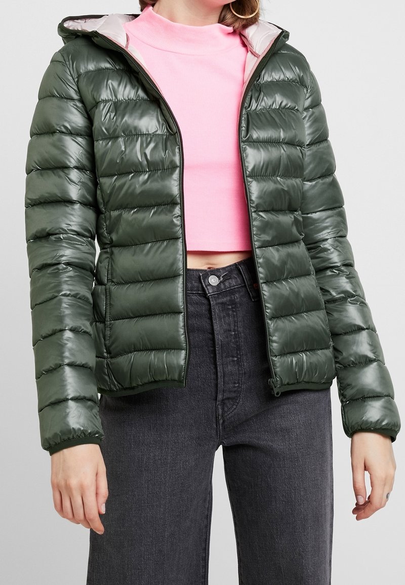 Mørkegrøn pufferjakke med en blank overflade og kviltet design, med lynlås foran og hætte med grå for. Båret over en lyserød top.