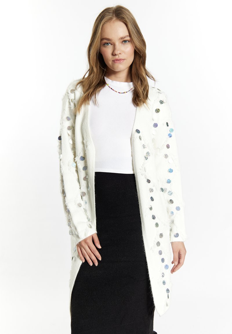 Cardigan bianco realizzato in un materiale morbido, con decorazioni circolari colorate e dettagli frangiati lungo i bordi.