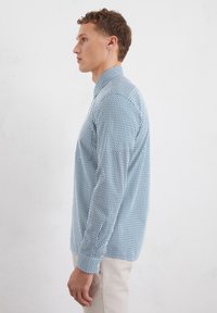 Light blue shirt with a geometric pattern, long sleeves, button-down collar, and a slim fit, worn with off-white trousers.