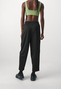 Pantaloni sportivi neri a vestibilità ampia, con vita elastica e dettaglio a striscia laterale, abbinati a un crop top verde e sneakers nere.