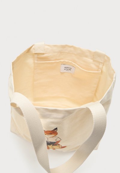 Sac tote en toile avec larges bretelles, poche intérieure, et illustration de renard sur le devant, montrant l'étiquette Maison Kitsuné Paris à l’intérieur.