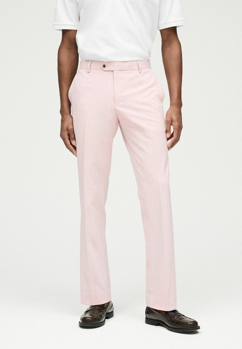Pantalones de vestir rosa claro con ajuste slim, textura sutil, cierre de un botón y bolsillos laterales, combinados con zapatos mocasines marrón oscuro.