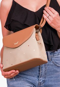 Beige kabela s hnědými uměloženými koženými akcenty; obsahuje puntíky v různých barvách; obdélníkový tvar s klopou a nastavitelným popruhem.