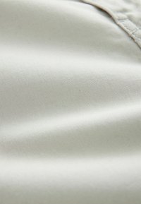 Tejido gris claro con una superficie suave y texturada que muestra finos patrones de tejido y un sutil brillo, adecuado para ropa o tapicería.