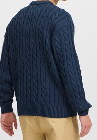 Pull en maille bleu marine avec motifs torsadés texturés, poignets et ourlet côtelés. Coupe ample, col rond et manches longues.