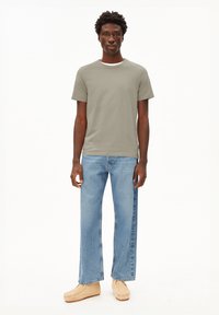 Olive green short-sleeve t-shirt with a white neckline, paired with light blue wide-leg jeans and beige slip-on shoes.