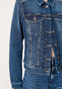 Jeansjacka i mörkblått med kontrasterande sömmar, bröstfickor och silverfärgade detaljer. Har en figursydd design och en strukturerad krage.