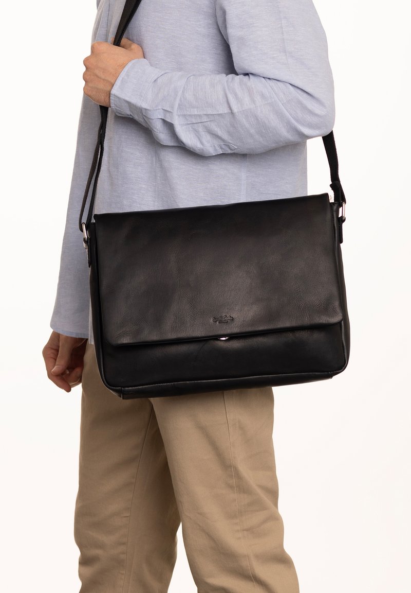 Black leather messenger bag with a smooth texture, magnetic flap closure, adjustable strap, and a subtle logo embossed on the front.