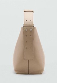 Bolso de mano beige con forma cónica, hecho de material suave. Presenta una correa ancha con múltiples agujeros y dos acentos de hardware plateado redondos.