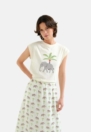 Mujer con camiseta blanca sin mangas con estampado de elefante y palmera y falda a juego con patrón de elefante y palmera.