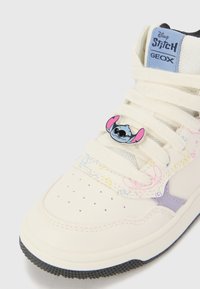 White high-top sneakers with geometric patterns, mesh detailing, and a blue tag. Features a Stitch character charm on the laces.