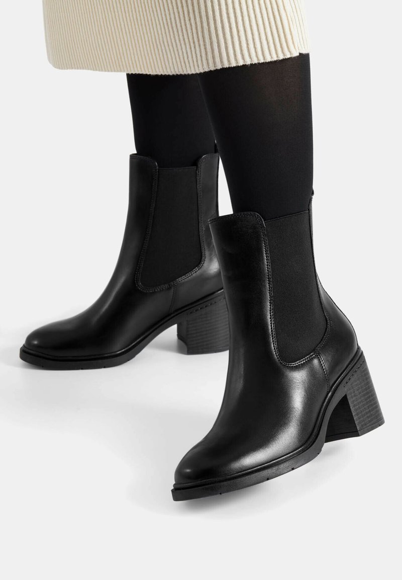 Black leather ankle boots with a block heel, featuring elastic side panels and smooth texture. Rubber sole for traction.