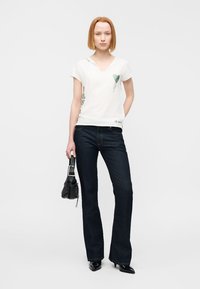 T-shirt blanc à manches courtes avec un motif de cœur vert et de plantes, associé à un jean évasé bleu foncé et un sac à main noir texturé.