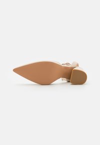 Nude høyhælte sko med spiss tå, gjennomsiktige stropper og en strukturert brun såle. Hælen har design i blokk for stabilitet.
