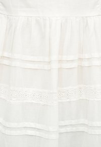 Λευκό υφασμάτινο στρώμα με πτυχώσεις και οριζόντια διακοσμητική δαντέλα.