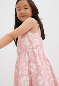 Rosa Blumenkleid mit ärmellosem Design, das weiße Blumenmuster, eine geraffte Taille und einen fließenden Rock aufweist.