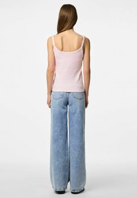 Top a tinta rosa chiaro aderente con spalline sottili abbinato a jeans in denim azzurro chiaro a vita alta e gamba larga. Sottile texture a costine sulla canotta.