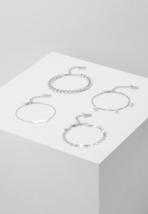 Fyra silverarmband visade på en vit yta. Inkluderar kedja, länk och accentdesign med varierande texturer och längder.