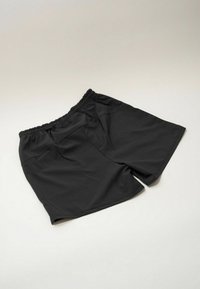 Shorts noirs à taille élastique étalés à plat sur une surface claire, montrant des poches avant et un détail à cordon.