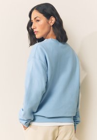Jasnoniebieska bluza z okrągłym dekoltem, opadającymi ramionami i ściągaczami na rękawach. Miękka tkanina o gładkiej fakturze, prezentująca luźny krój.