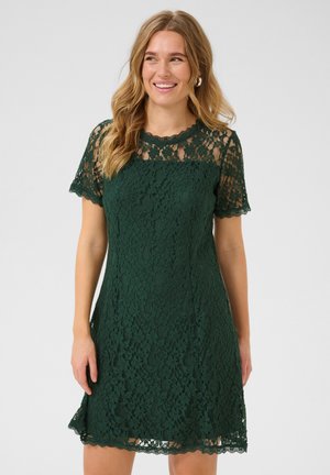 Green lace dress with a scalloped neckline and short sleeves, featuring a textured floral pattern and a fitted silhouette.